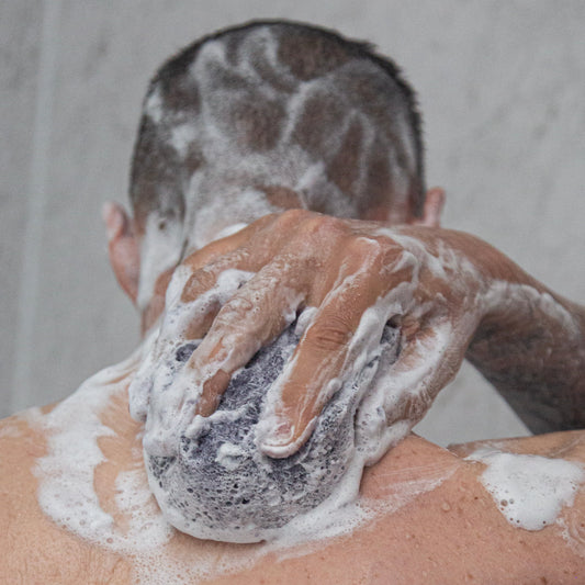 Person applying soap to their back with a bar of soap.