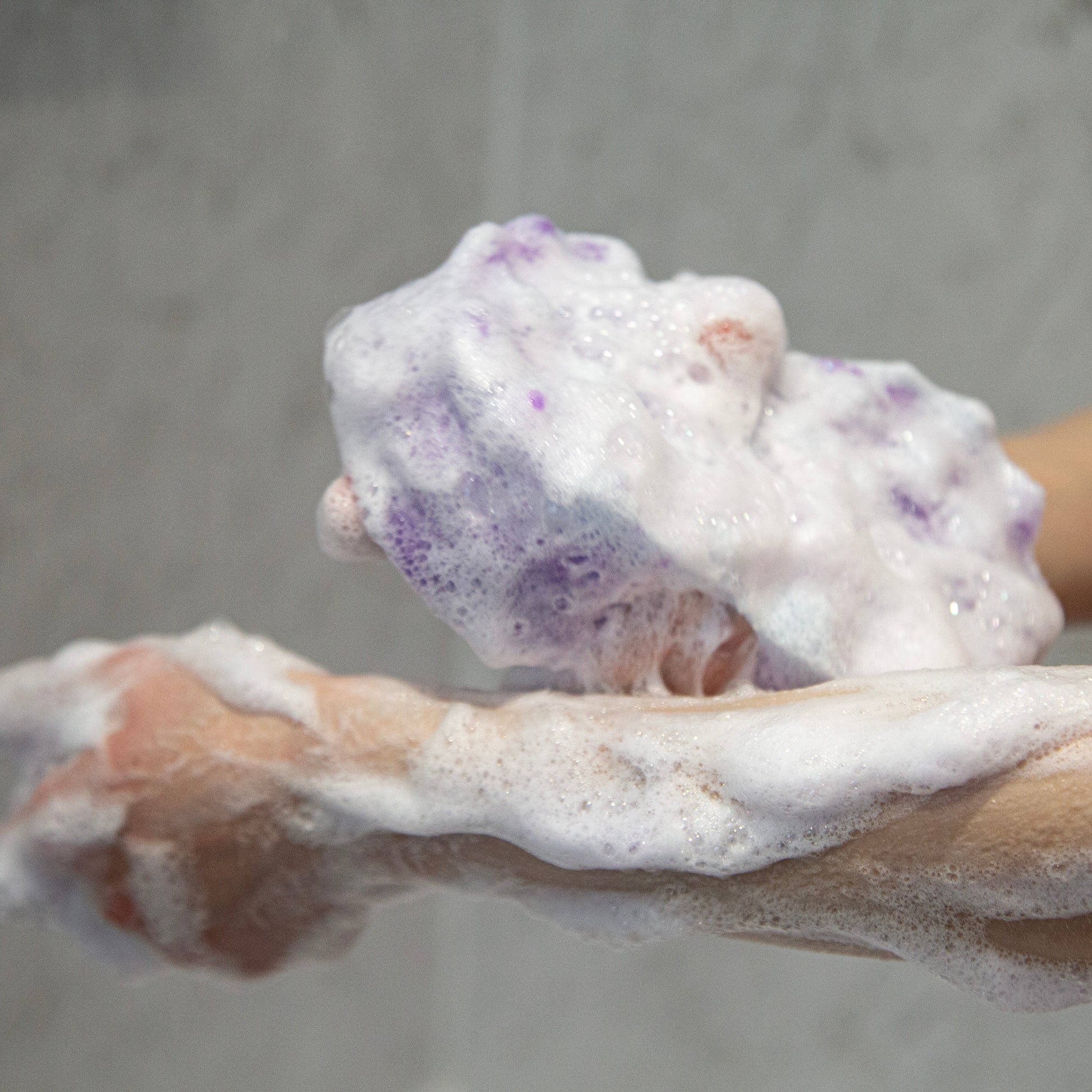 Hand holding a lathered bar of black opium soap with a gray background