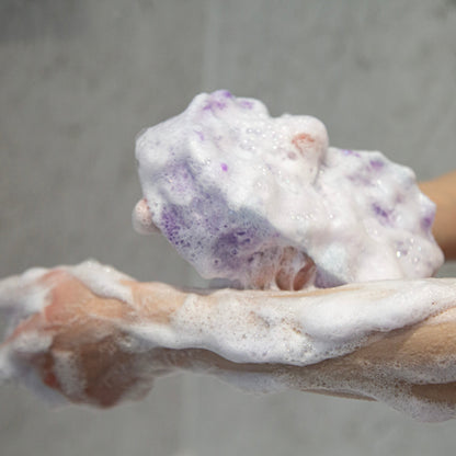 Hand holding a lathered bar of black opium soap with a gray background