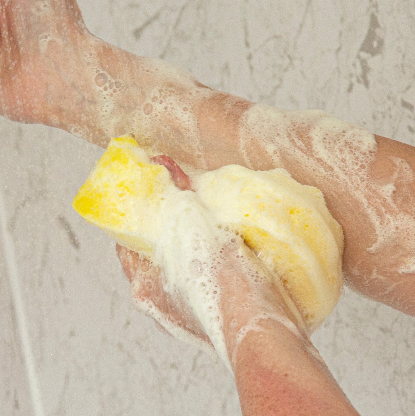 Person scrubbing their arm with a yellow exfoliating sponge  on a light gray background
