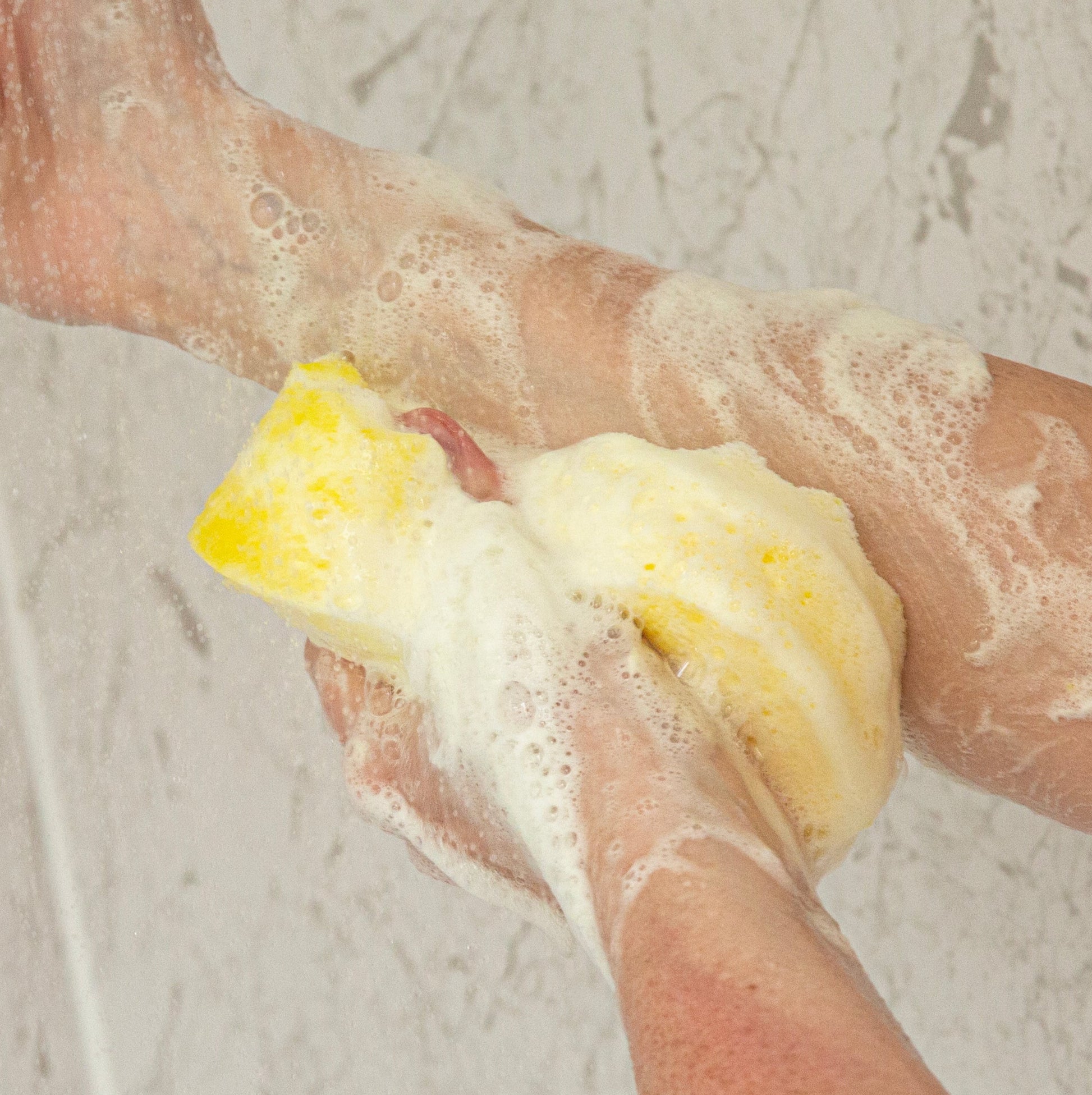 Person scrubbing their arm with a yellow exfoliating sponge  on a light gray background