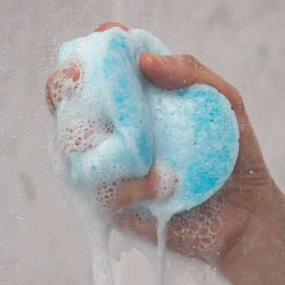 Hand holding a blue and white foamy bath bomb against a gray background